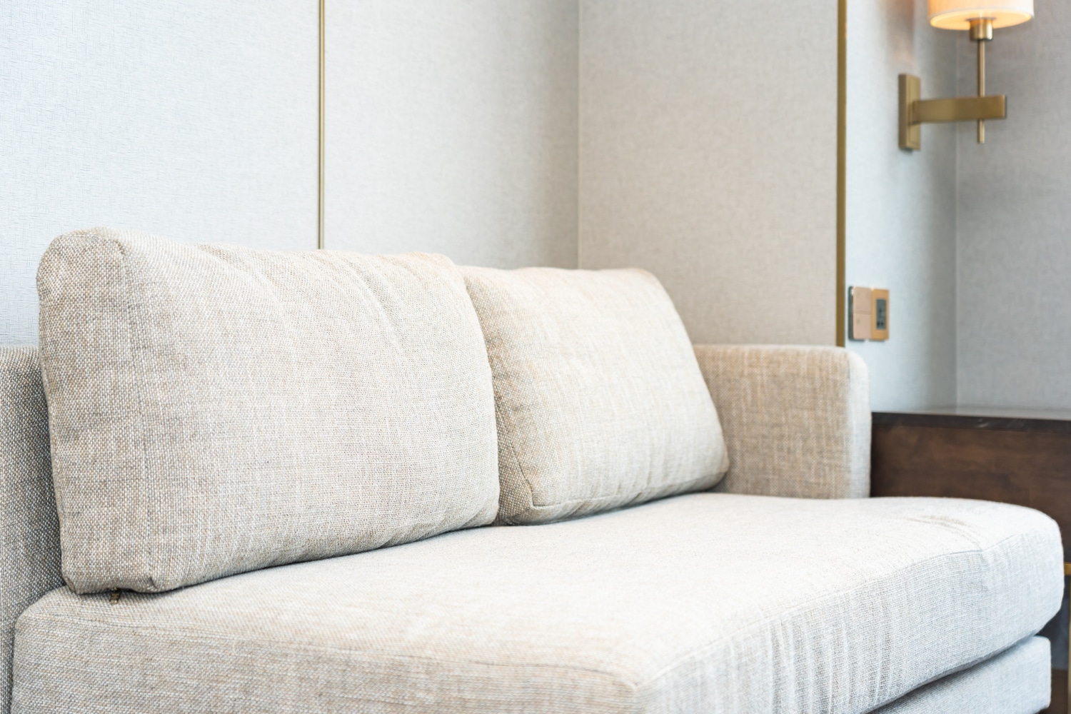 Canapé moderne beige avec des coussins texturés, placé dans un salon lumineux et minimaliste avec une lumière élégante et des murs de couleur claire.