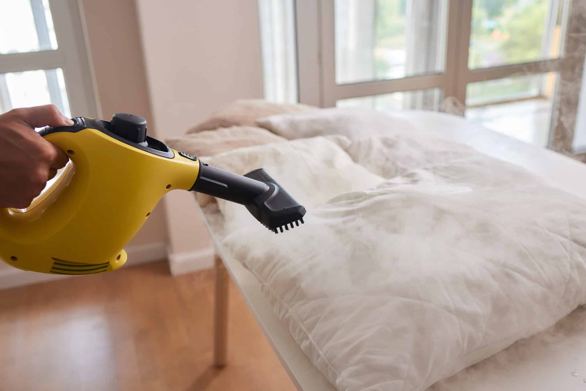 Nettoyage d'une couette avec un nettoyeur vapeur portatif jaune dans une chambre lumineuse.